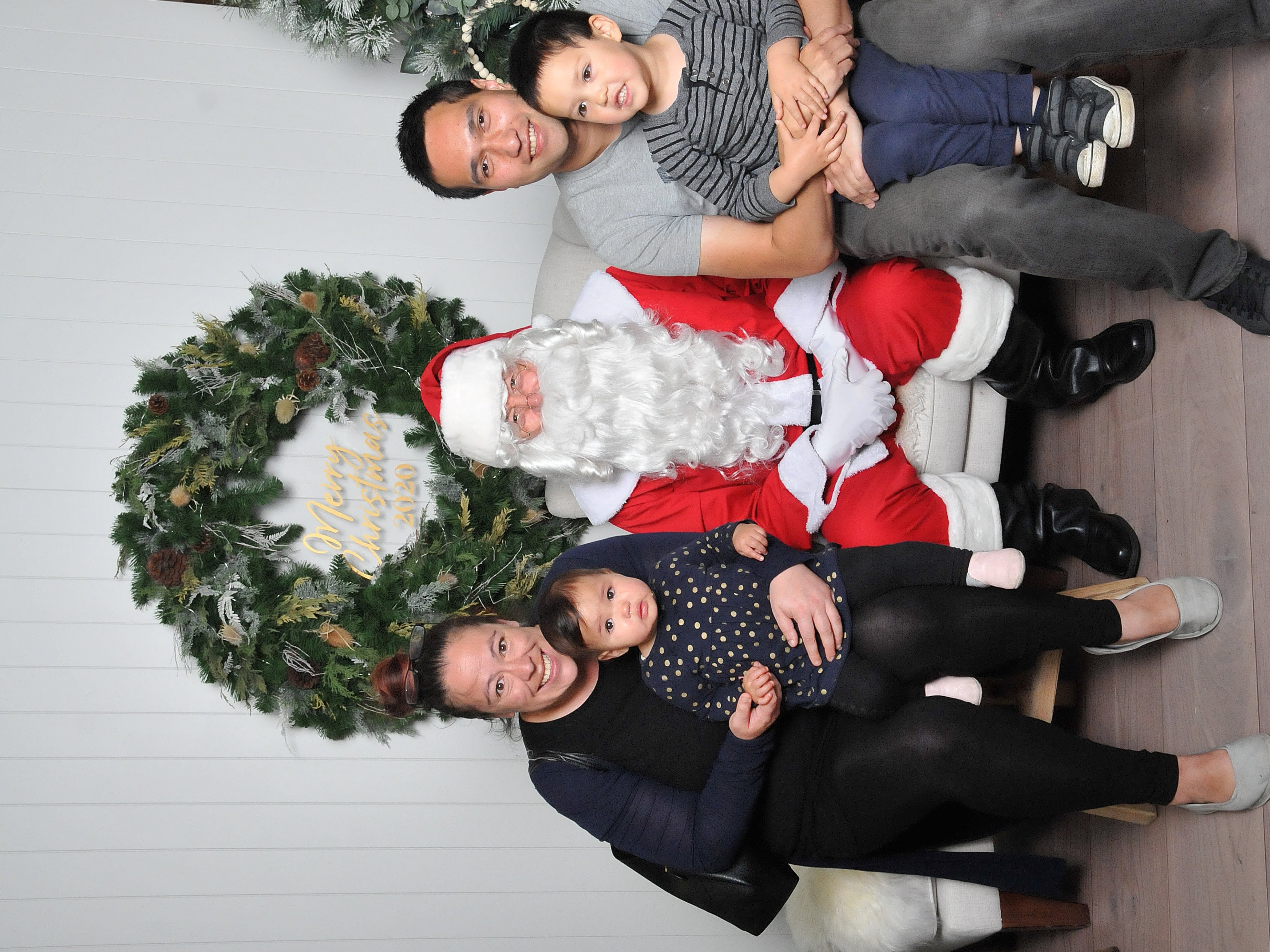 Santa is sat between a father holding his child on his lap and a mum with her little girl on her lap. All are smiling.