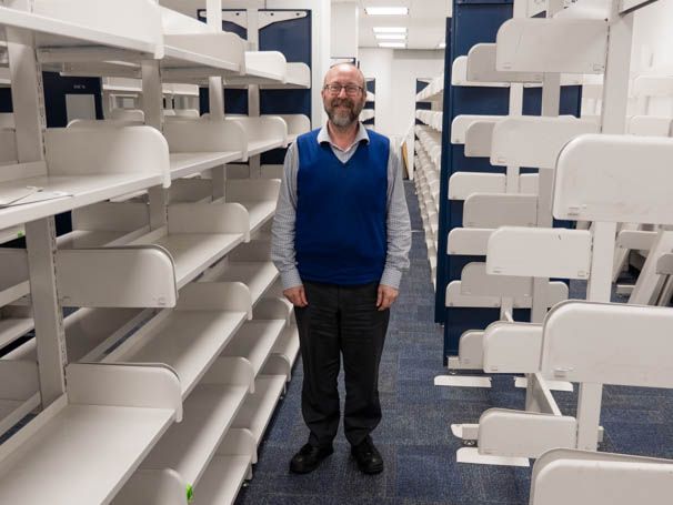 Robin Anderson stands beside empty library shelves