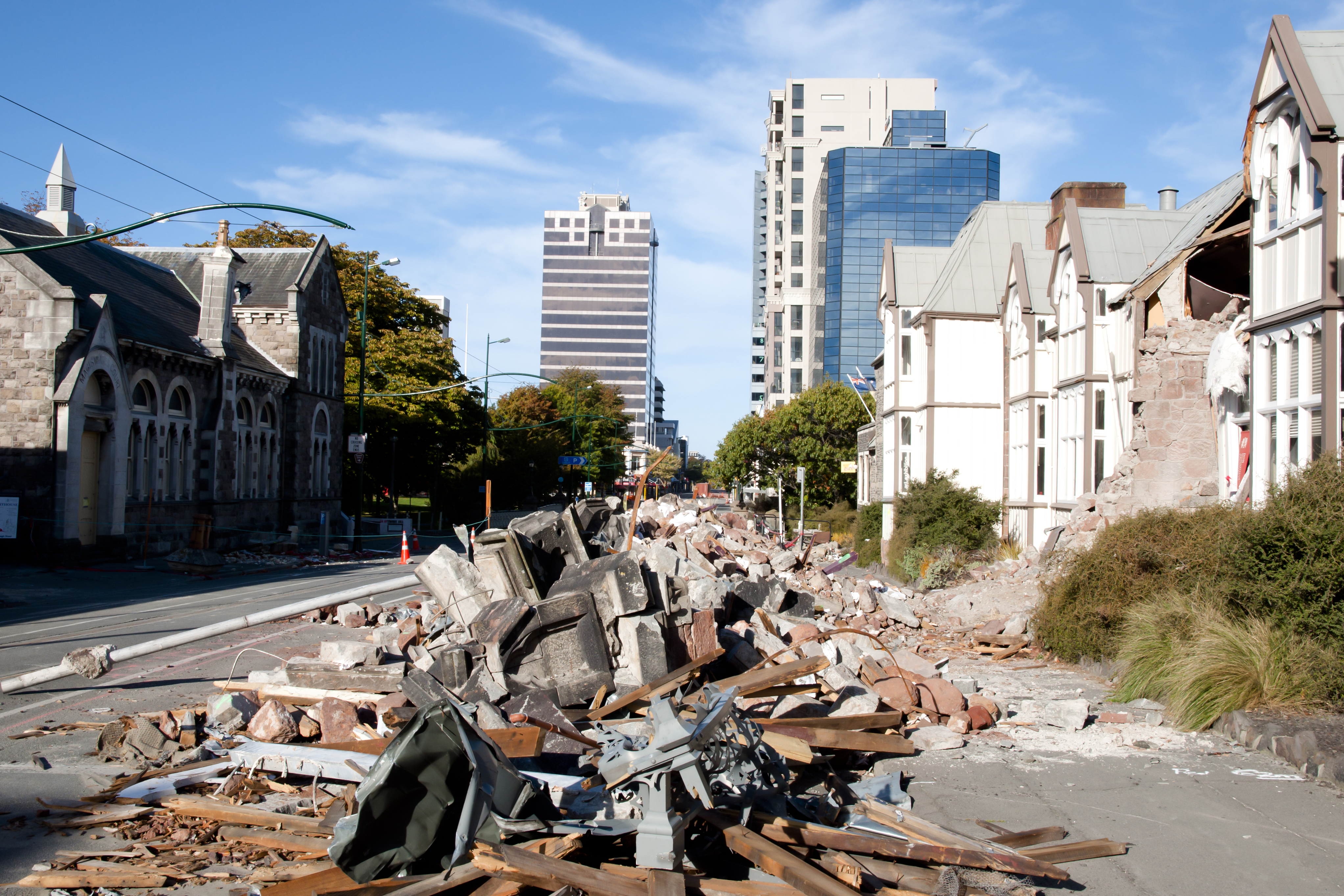 Pile of rubble in the street, houses with the front falling down due to earthquake. Office towers in the background.